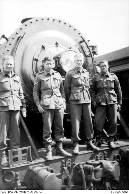 Quorn, SA. 11 October 1941. Group portrait of four members of A Company, 2/4th Machine Gun Battalion in front of a train locomotive en route from Woodside camp to Alice Springs. From left to right: Charlie Parke, WX7007 Edward George (Eddie) Burton (died of illness on 21 February 1945 in Sandakan, Borneo, whilst a Prisoner of War (POW)), A. S. Parke, unidentified.